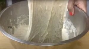 Hands stretching sticky dough in a metal mixing bowl.