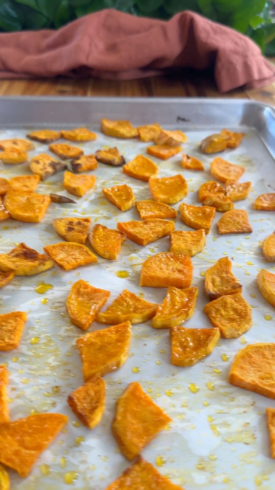 Baked sweet potato slices on a baking sheet with a cloth in the background.