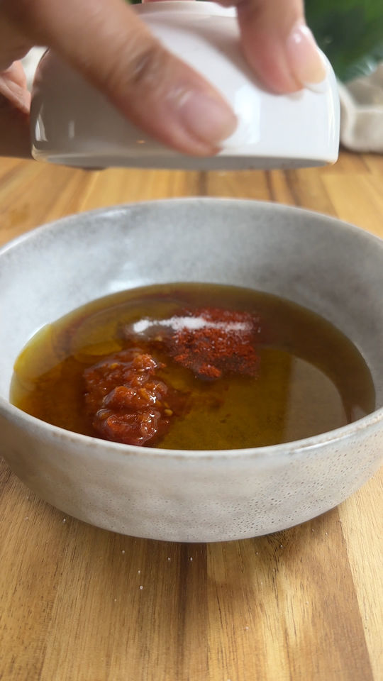 Hand mixing oil, harissa, and spices on wooden surface.