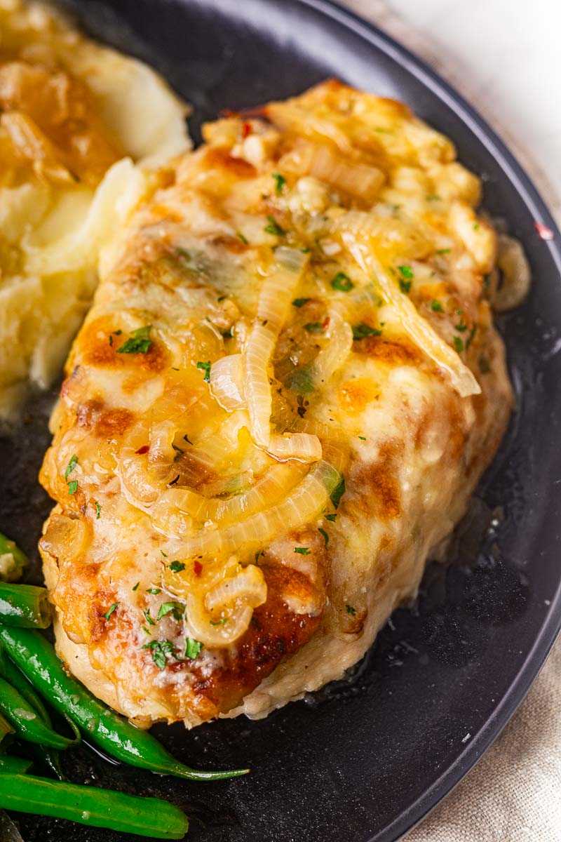 French onion soup chicken with caramelized onions, served with mashed potatoes and green beans on a black plate.
