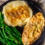 French onion soup chicken with caramelized onions, mashed potatoes, and green beans on a black plate.