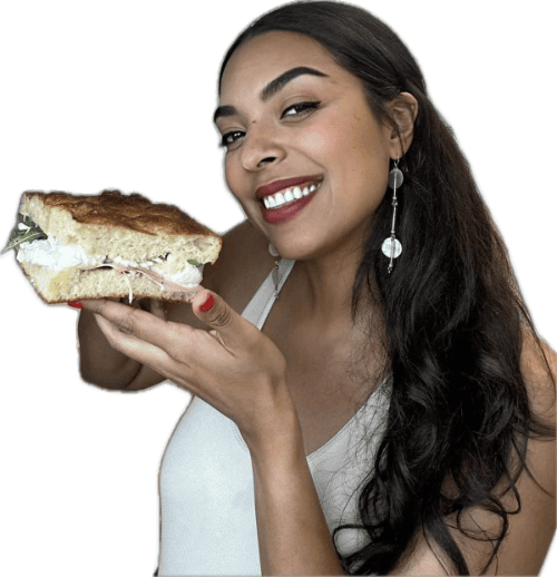 Smiling woman holding a large sandwich with layers of meat and lettuce.