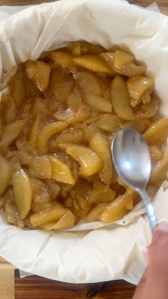 Person preparing apple pie filling in a pastry-lined dish with a spoon.