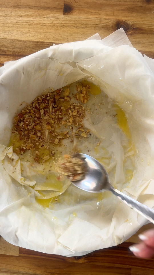 Spoon spreading chopped nuts and butter in a parchment-lined baking dish on a wooden surface.