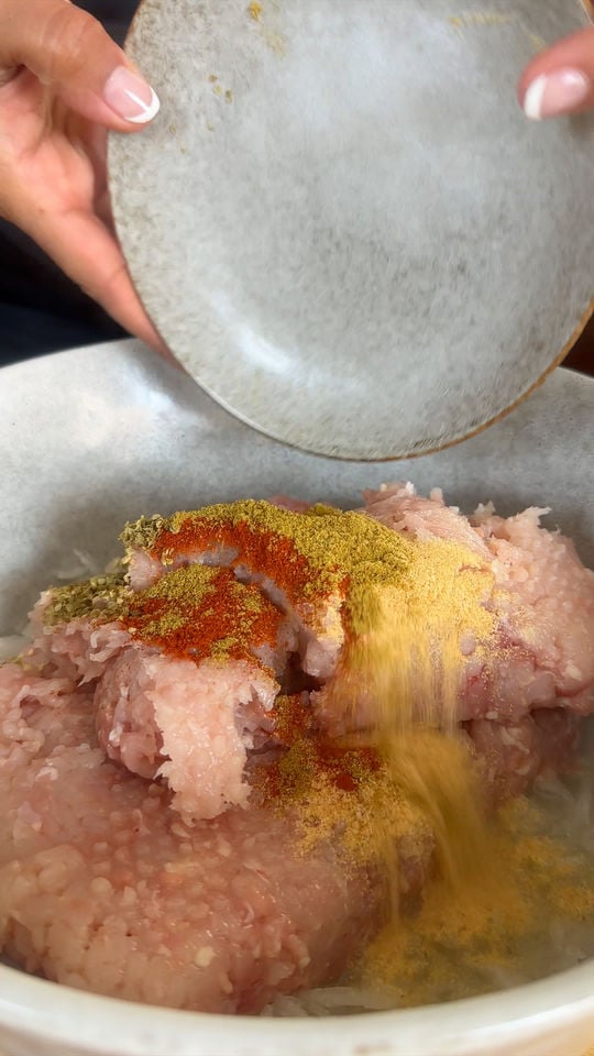 Adding spices to ground meat in a bowl for cooking.