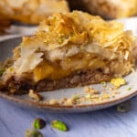 A slice of apple pie baklava with flaky phyllo layers, honey, and crushed pistachios on a plate.