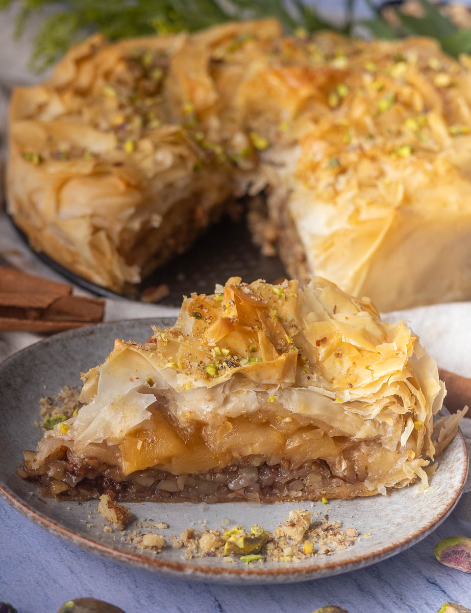 Slice of apple pie  baklava on a plate with layers of phyllo pastry, nuts, and honey, garnished with crushed pistachios.