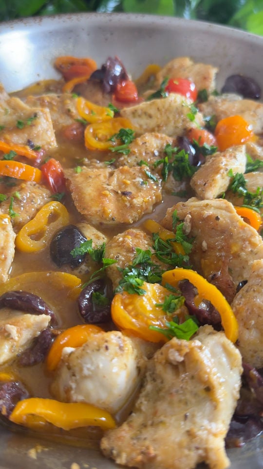 Chicken cooked with olives, cherry tomatoes, bell peppers, and herbs in a skillet.