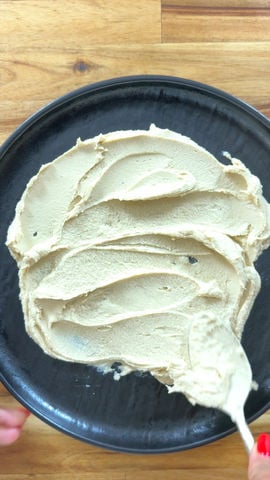 Smooth hummus spread on a dark plate with a spoon, on a wooden table.
