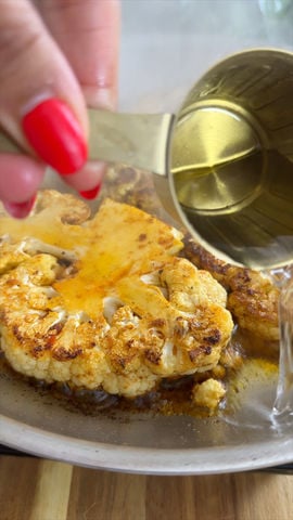 Pouring water over a roasted cauliflower steak in a pan.