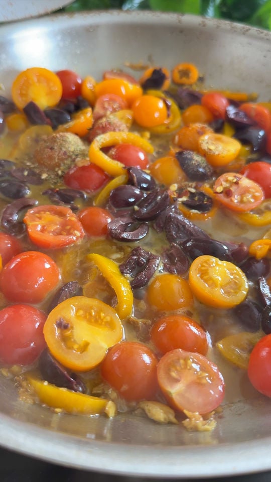 Sautéed cherry tomatoes, olives, and bell peppers in a pan.