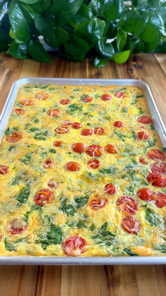 Cooked Eggs with cherry tomatoes, spinach, and cheese in a pan on a wooden table.