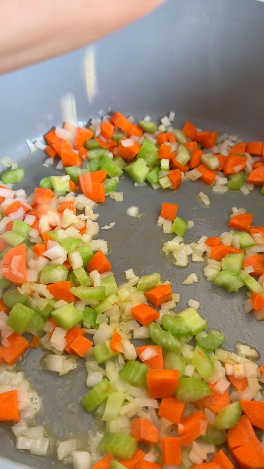 Chopped carrots, celery, and onions being sautéed in a pan.