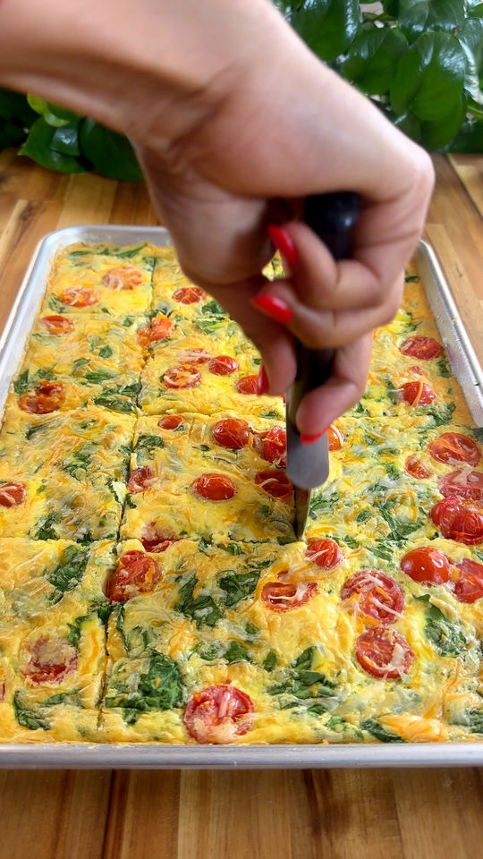 Hand cutting a eggs with cherry tomatoes and spinach on a baking sheet.
