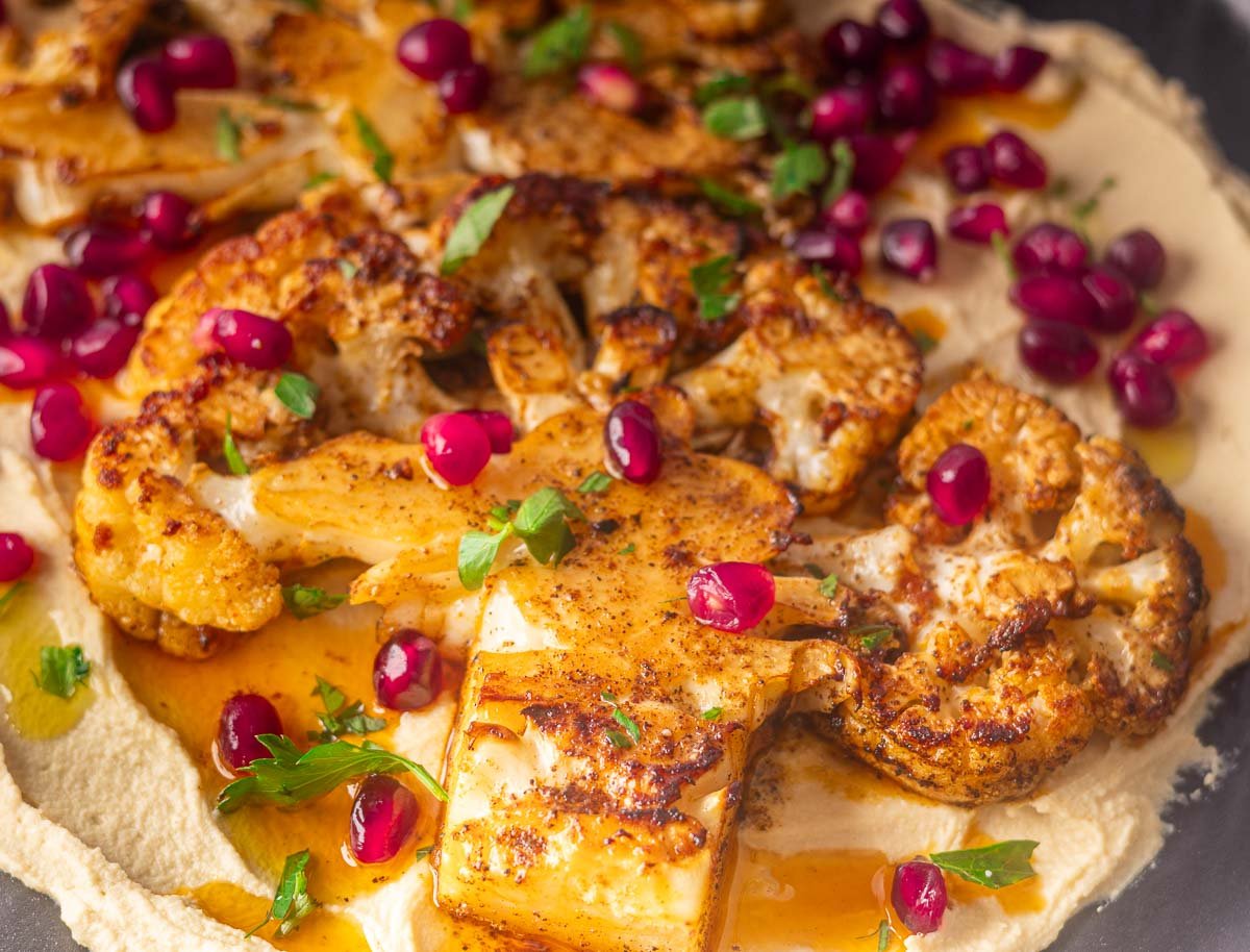 Pan-seared cauliflower steaks on creamy hummus, garnished with pomegranate seeds and parsley.