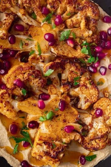 Pan-seared cauliflower steaks on hummus, garnished with pomegranate seeds and parsley.
