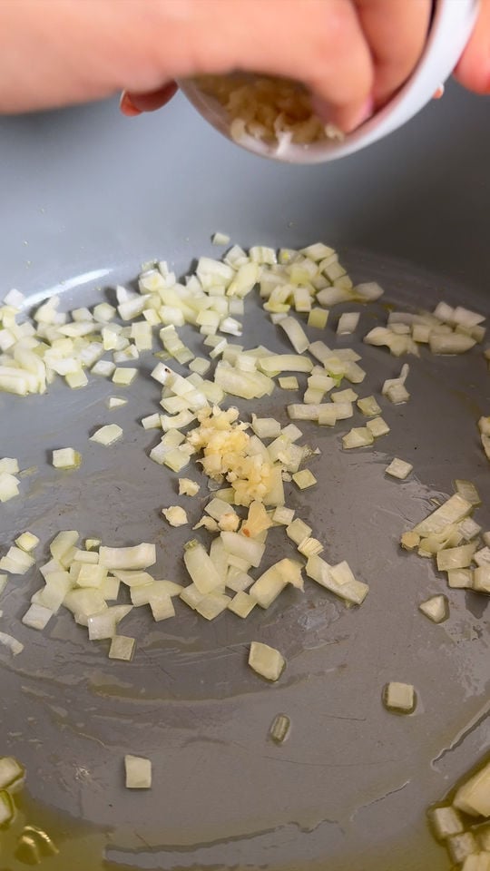 Chopped onions and minced garlic being added to a pan with oil for sautéing.