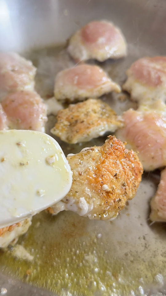 Chicken pieces frying in a pan, with a spatula flipping a golden-brown piece.