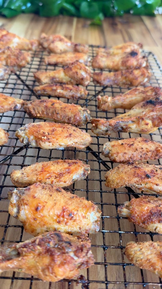 Grilled chicken wings on a cooling rack with green leaves in the background.