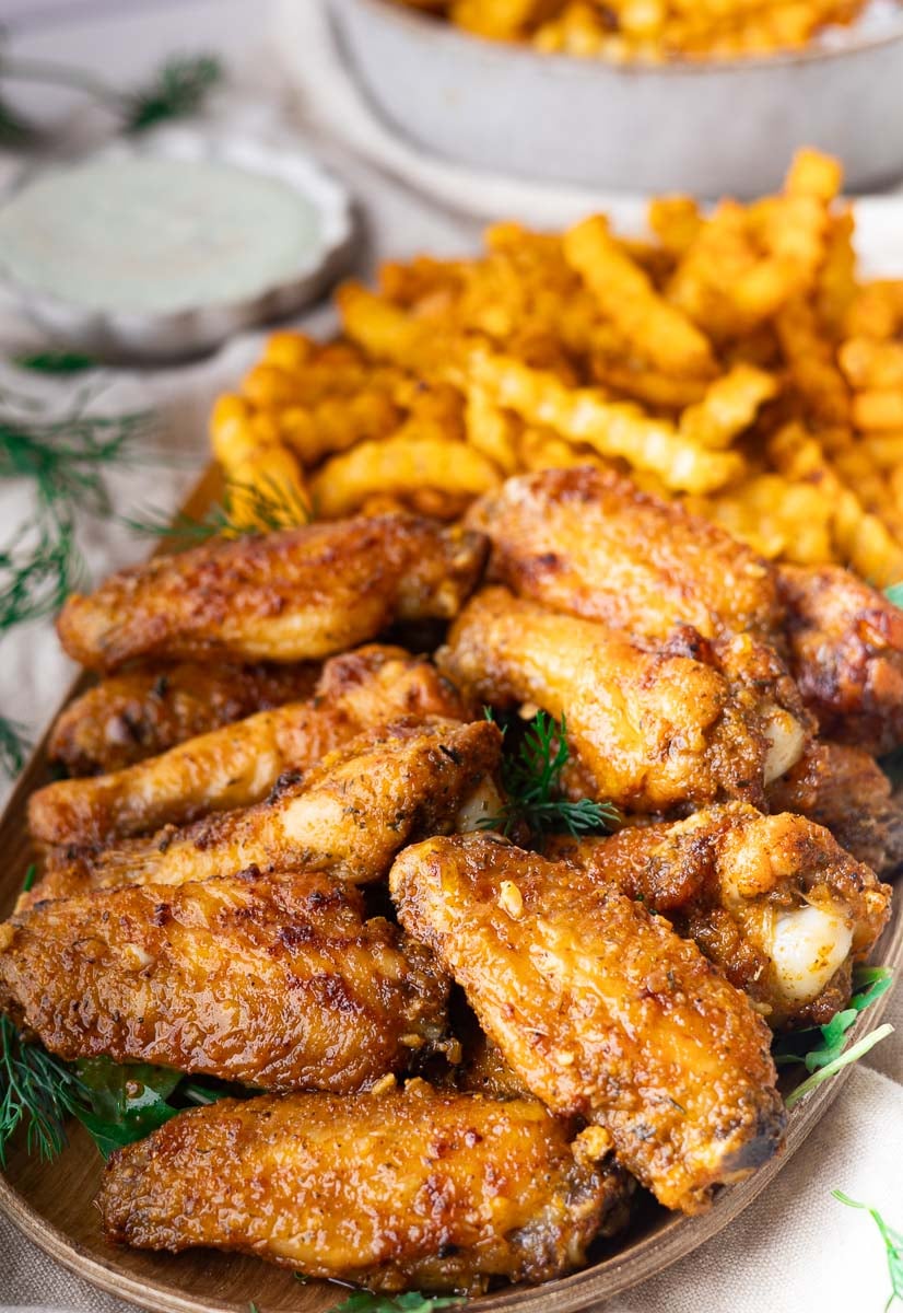 Crispy Mediterranean baked wings with crinkle-cut fries and ranch dip on a wooden platter.