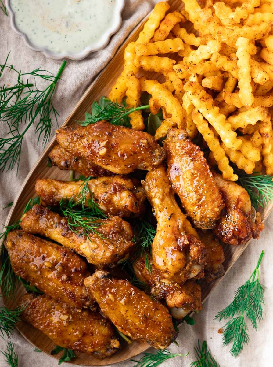 Crispy Mediterranean baked wings with seasoning, crinkle-cut fries, and dill garnish on a wooden platter.