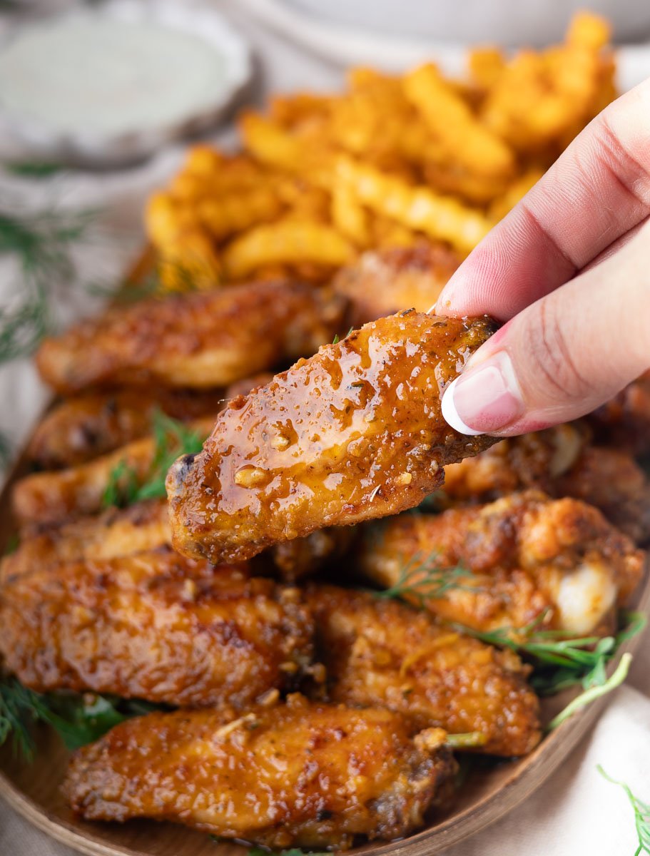 Hand holding Crispy Mediterranean baked wings with fries in background.