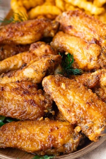 Crispy Mediterranean baked wings on a wooden platter with garnish and crinkle-cut fries in the background.
