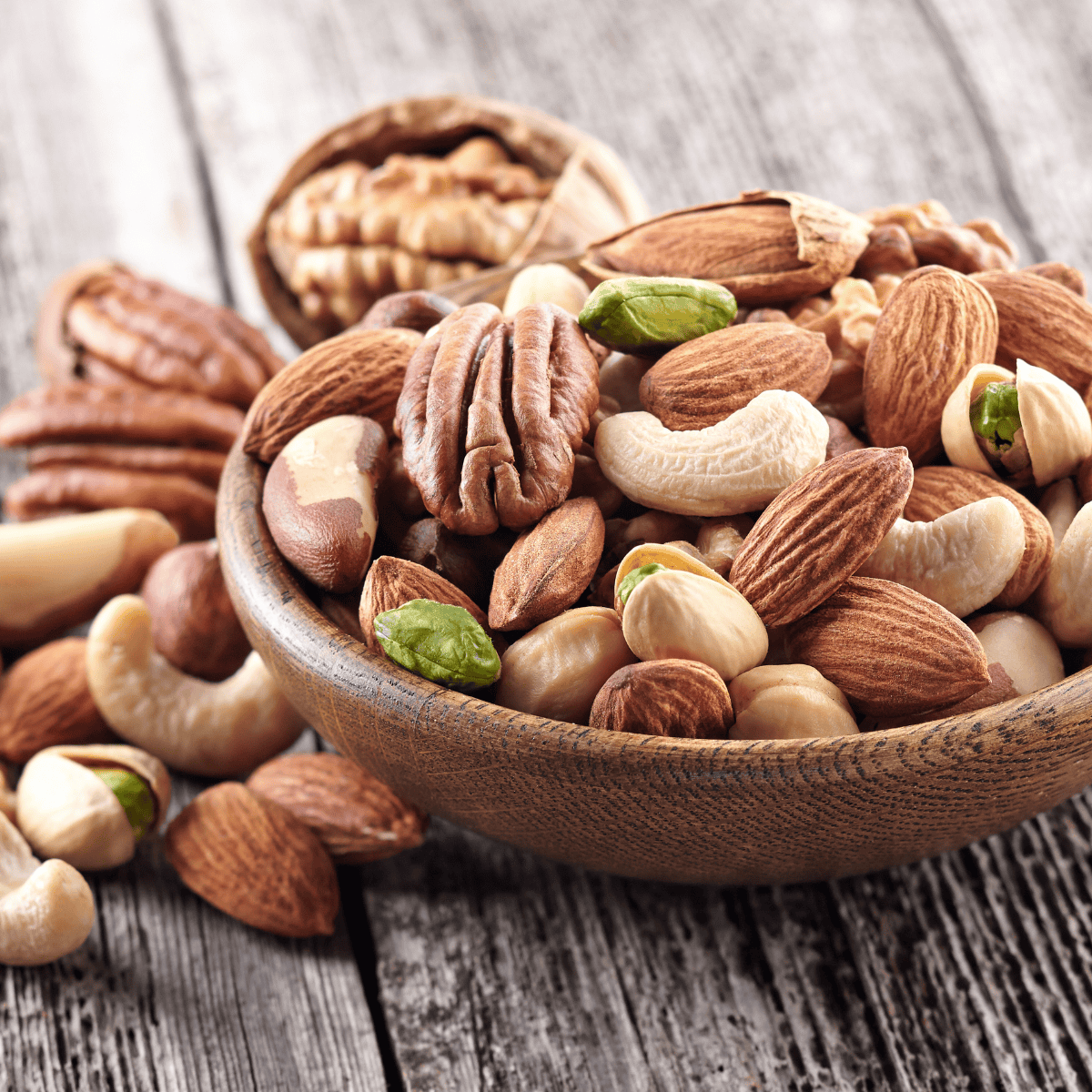 Assorted nuts in a wooden bowl on rustic wooden surface.
