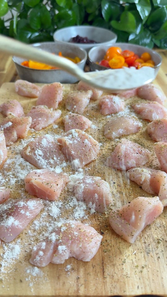 Raw chicken pieces seasoned with flour and herbs on a cutting board, with bowls of vegetables in the background.