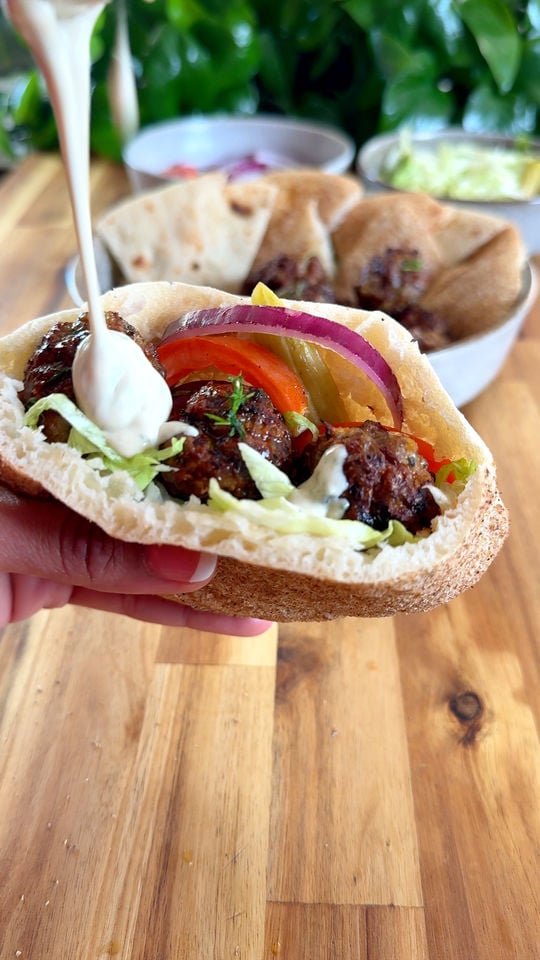 Pita with meatballs, lettuce, tomatoes, and red onion, topped with sauce.