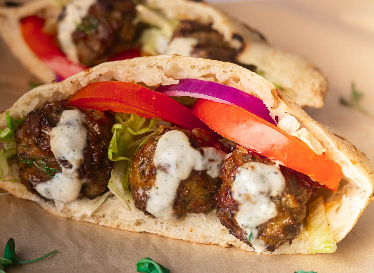 Spiced lamb meatballs with lettuce, tomatoes, red onion, and white sauce on a paper background.