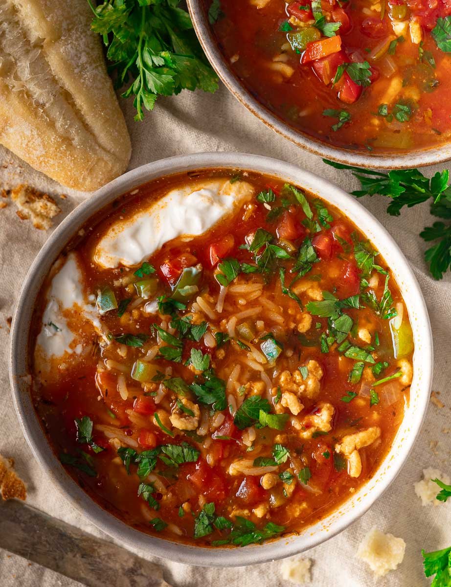 Bowl of stuffed pepper soup with chopped herbs and cream, served with crusty bread on a cloth surface.