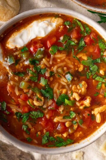 Bowl of stuffed pepper soup with rice, ground meat, diced vegetables, and fresh parsley on top.
