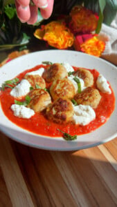 Plate of meatballs with red sauce, ricotta, and basil on a wooden table background.