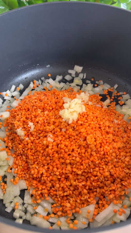 Chopped onions, red lentils, and minced garlic in a black pot.