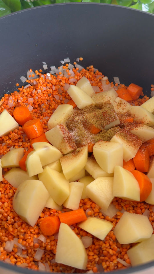 Chopped potatoes, carrots, lentils, onions, and spices in a pot.