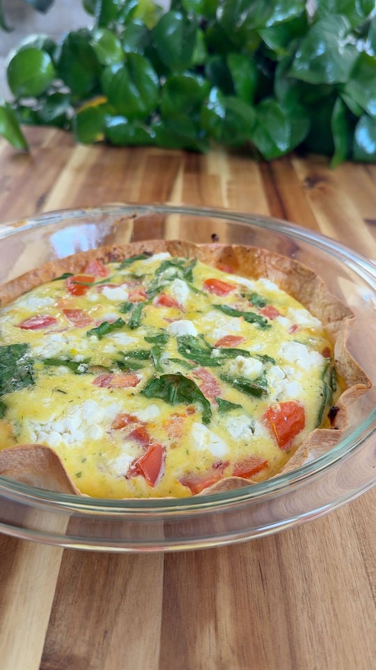 Vegetable and cheese eggs in a glass dish on a wooden table.