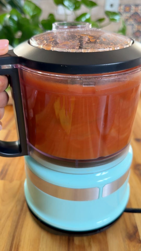 Blue food processor blending red sauce on wooden counter.