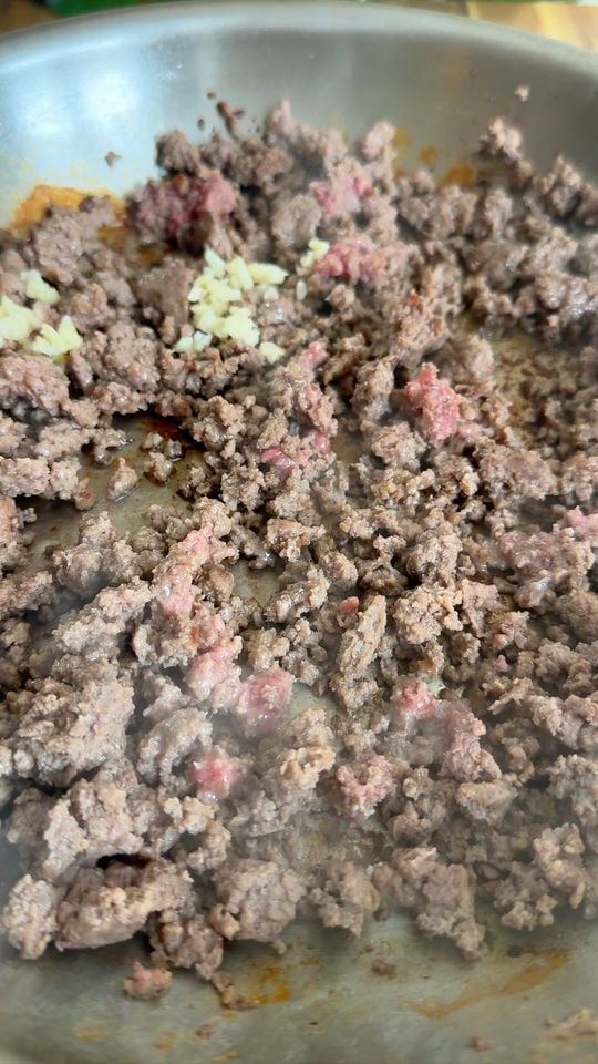 Ground beef with minced garlic cooking in a skillet.