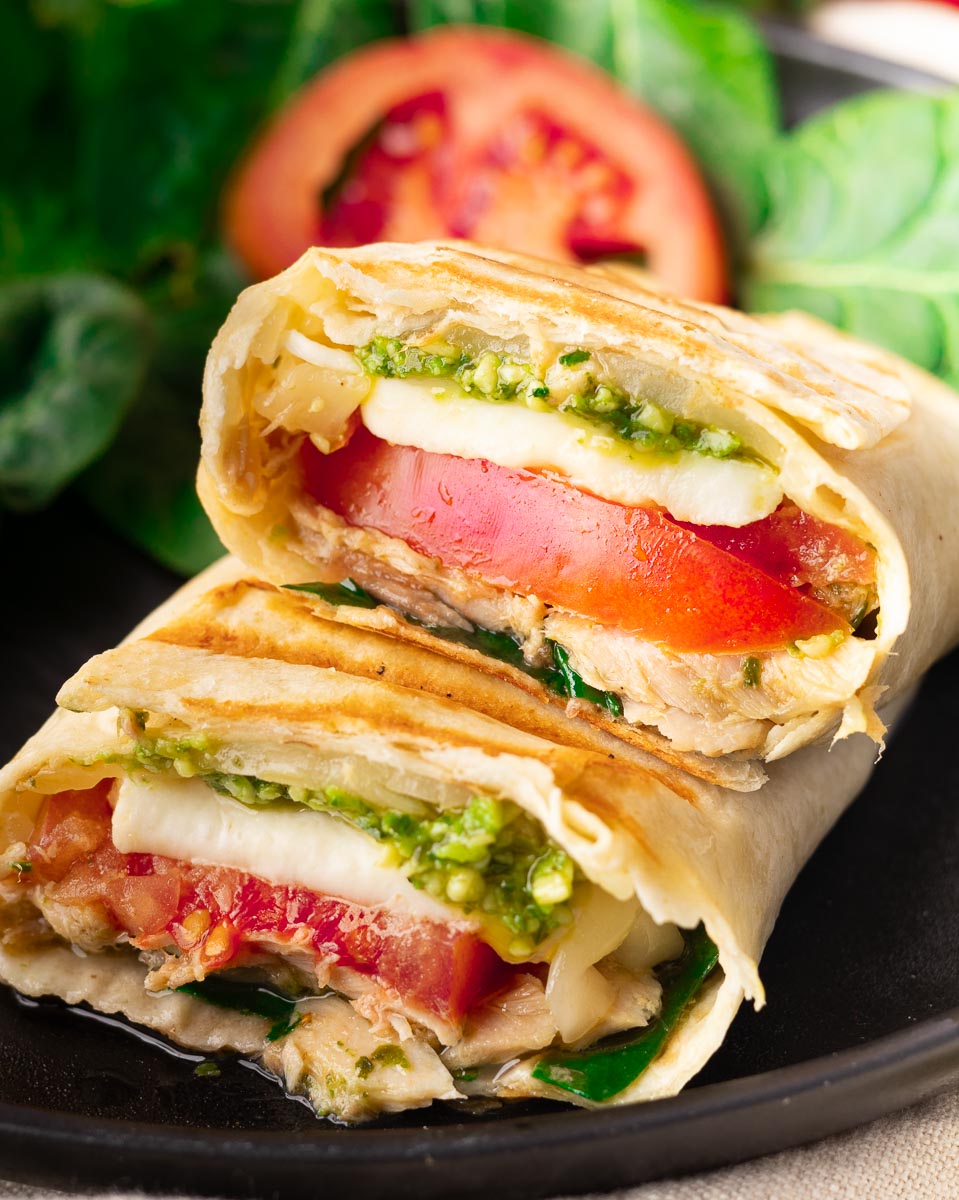 Caprese tuna melt wrap wrap with tomato, mozzarella, and pesto, served with salad greens on a black plate.