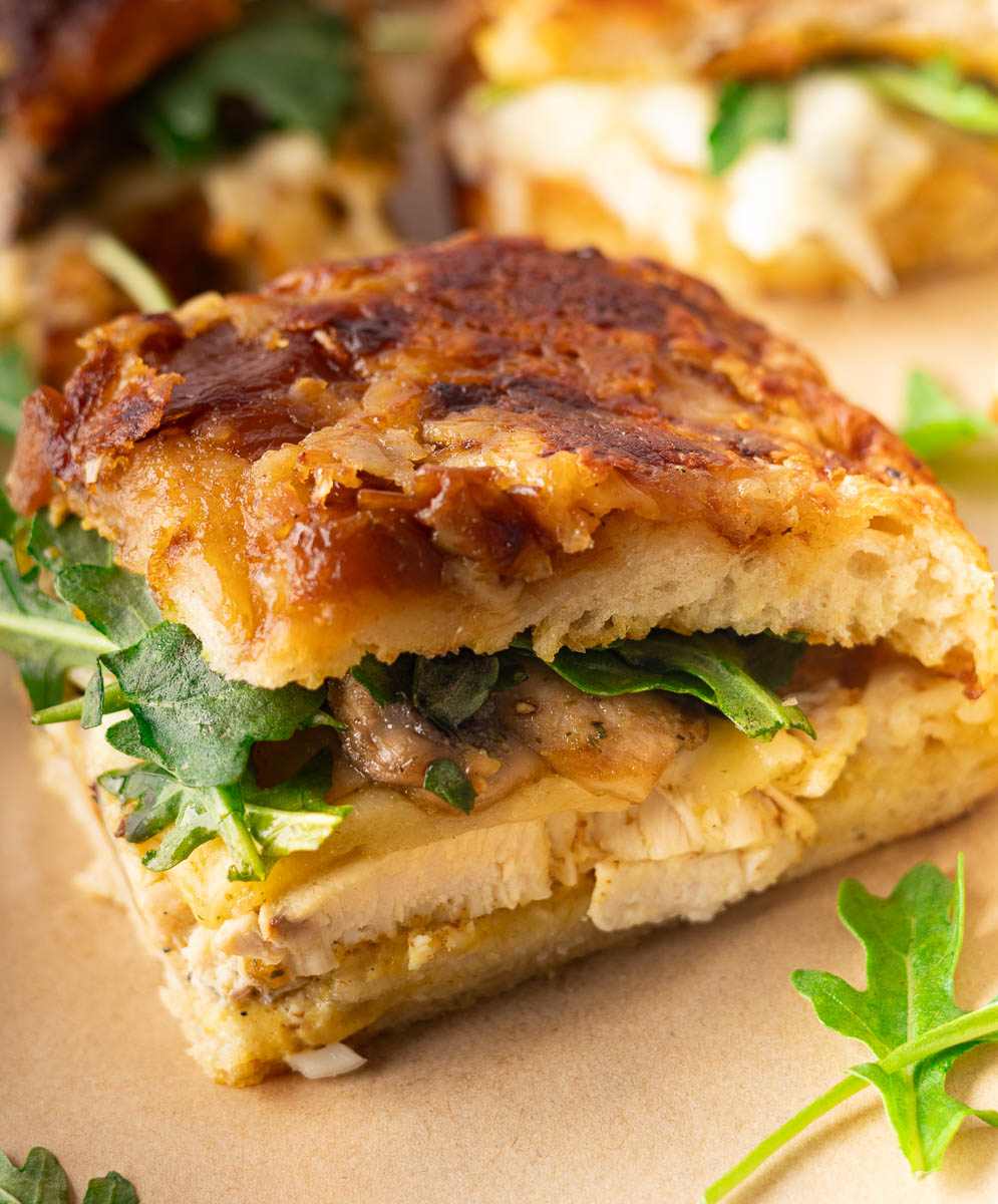 Caramelized Onion Focaccia Chicken Sandwich with chicken, arugula, melted cheese, and caramelized onions on toasted bread.
