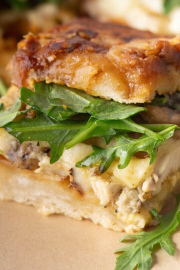 Close-up of a panini sandwich with arugula, melted cheese, and crispy toasted bread.
