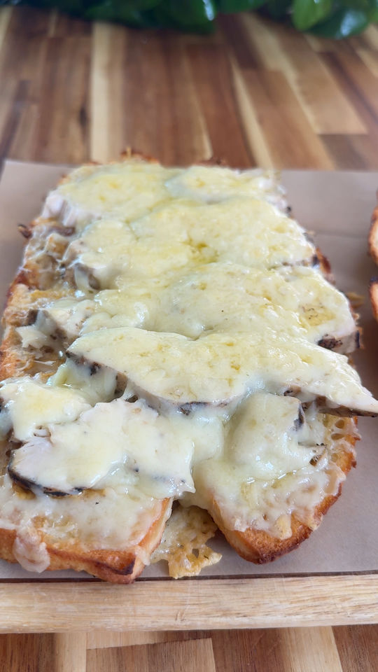 Melted cheese on sliced bread on a wooden board.