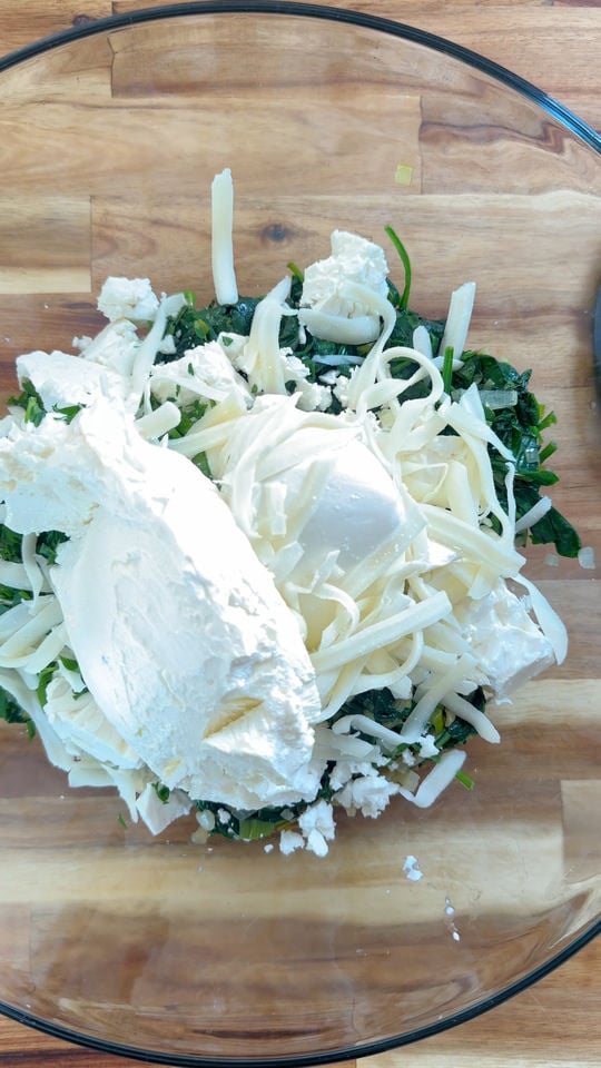 Bowl with spinach, ricotta, and grated mozzarella on a wooden surface.