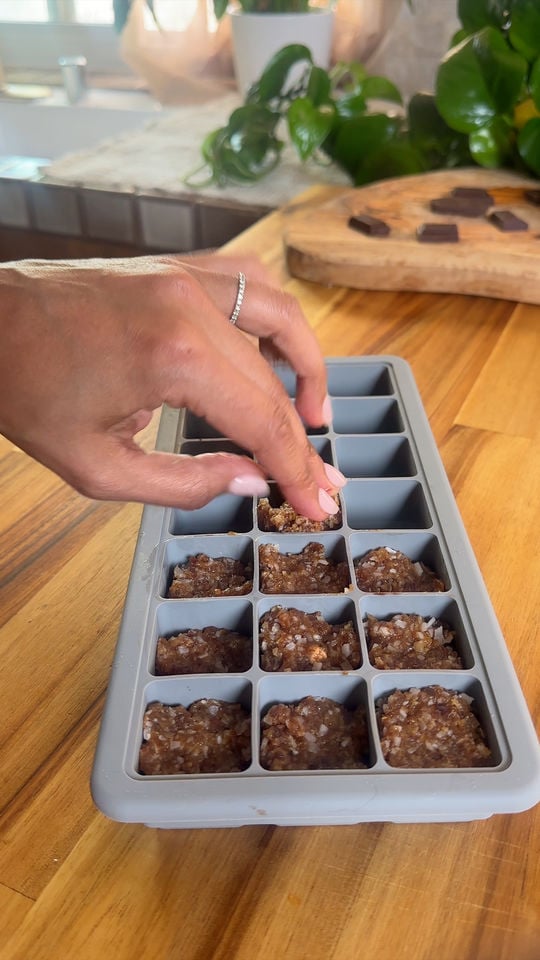 Hand placing filling into a silicone mold on a wooden countertop with plants in the background.
