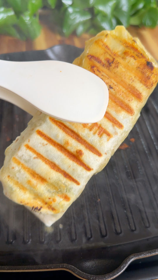 Grilled wrap being pressed with a spatula on a grill pan with char marks.