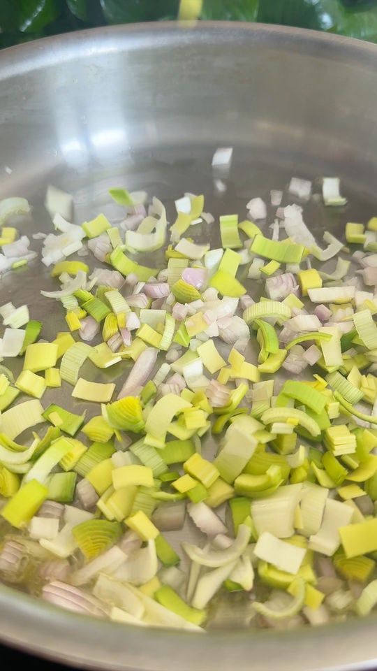 Chopped leeks and onions cooking in a stainless steel pan.