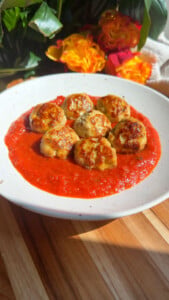 Meatballs in tomato sauce on a white plate with vibrant floral background.