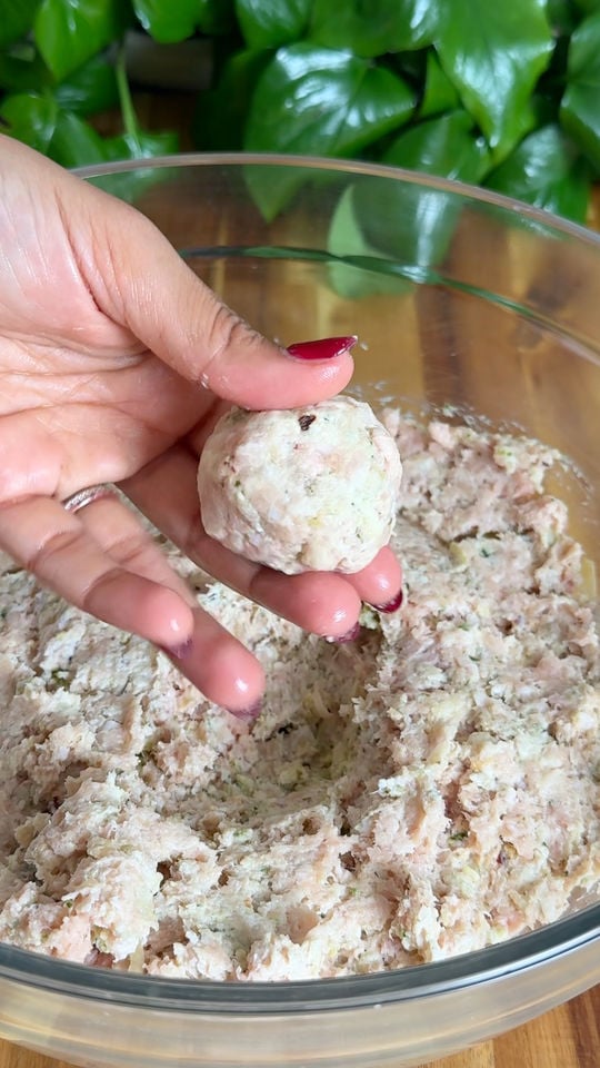 Hand holding a meatball above a bowl of minced meat mixture.
