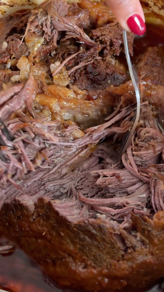 Close-up of shredded beef being pulled apart with a fork in a rich, brown sauce.